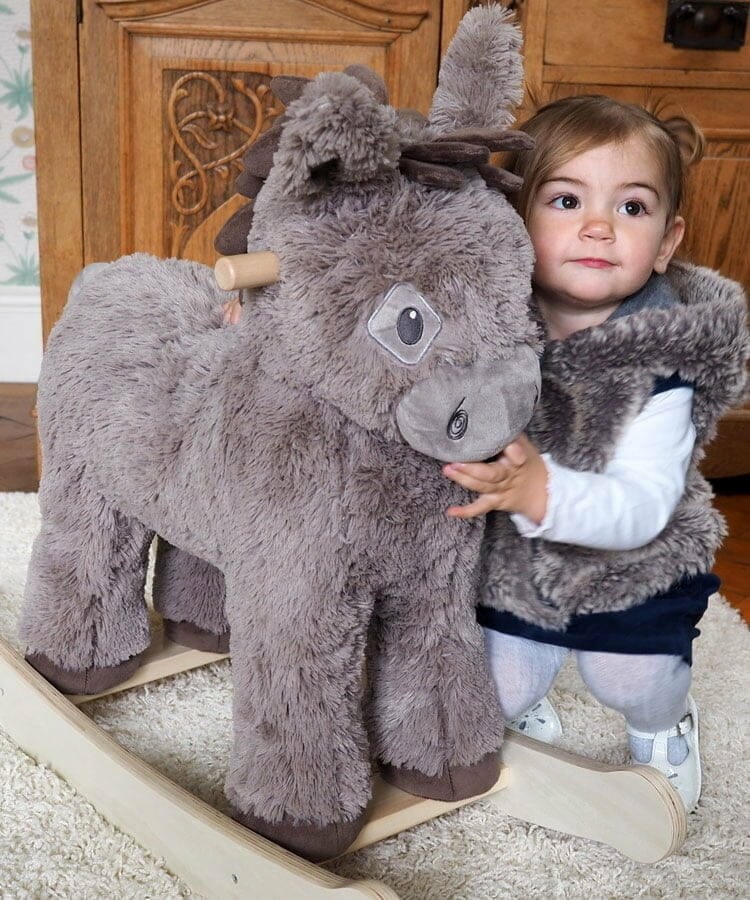 Grey plush rocking donkey with cute face and handles, toddler kneeling beside