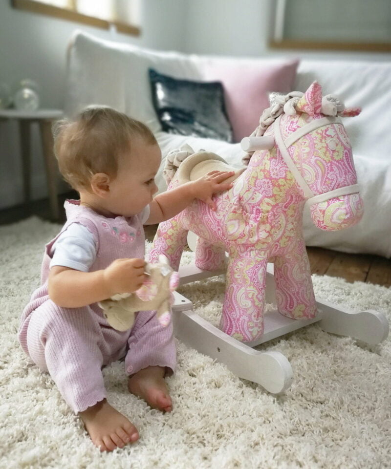 Baby girl playing with paisley pink Pixie & Fluff Rocking Horse on a cream rug