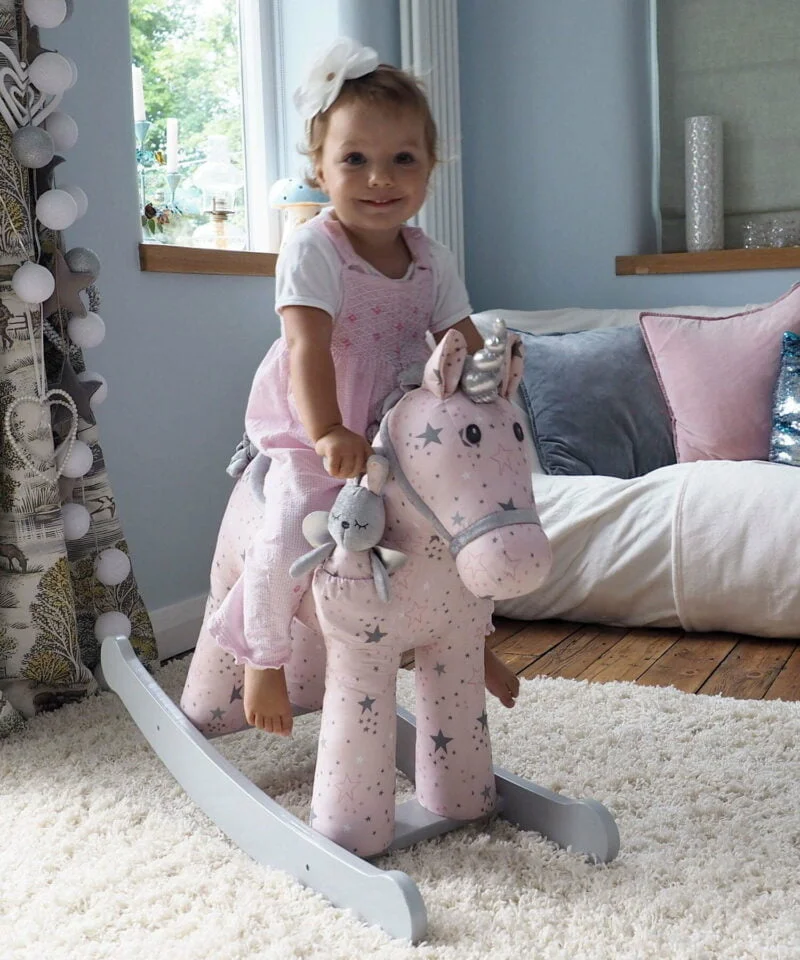 Toddler riding a Celeste & Fae Rocking hrse unicorn with pink star print fabric