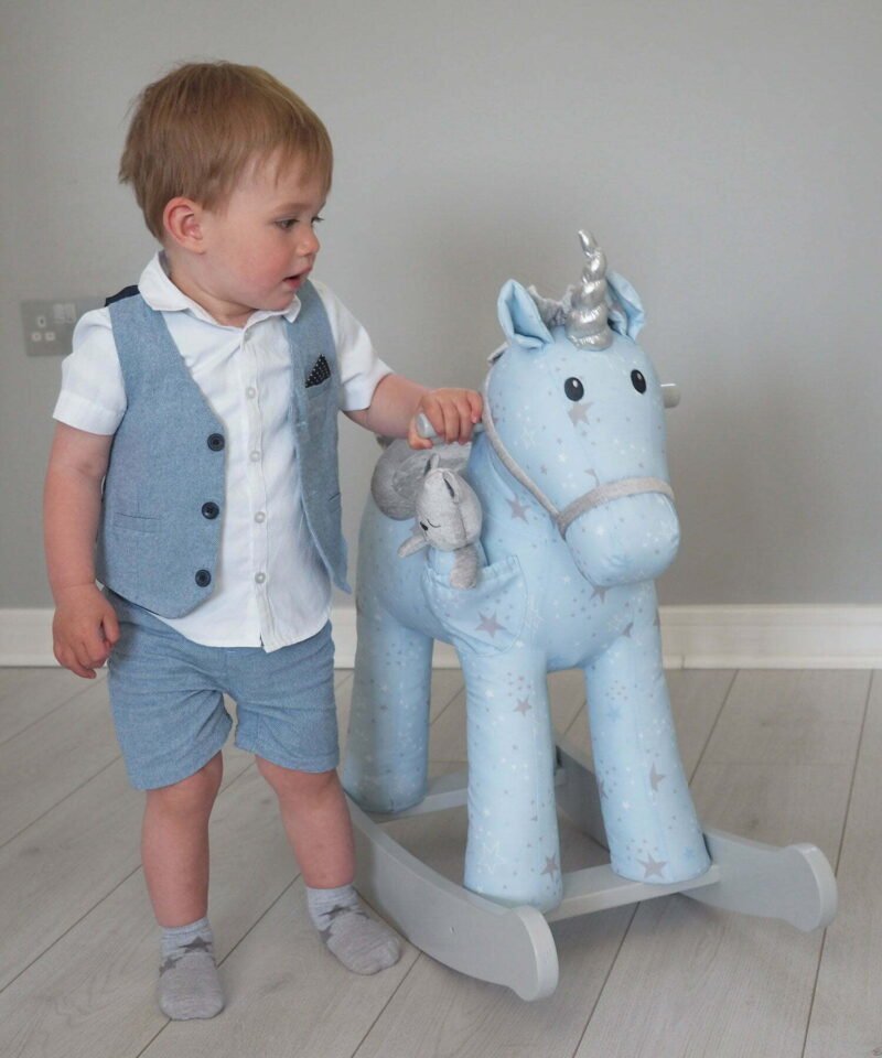 Little boy standing with blue Moonbeam & Rae Rocking Unicorn with grey painted rocking rails