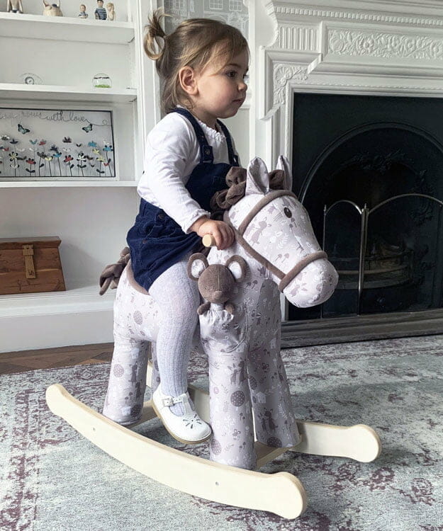 Little girl in blue dress riding luxury Biscuit & Skip Rocking Horse with sturdy wooden frame