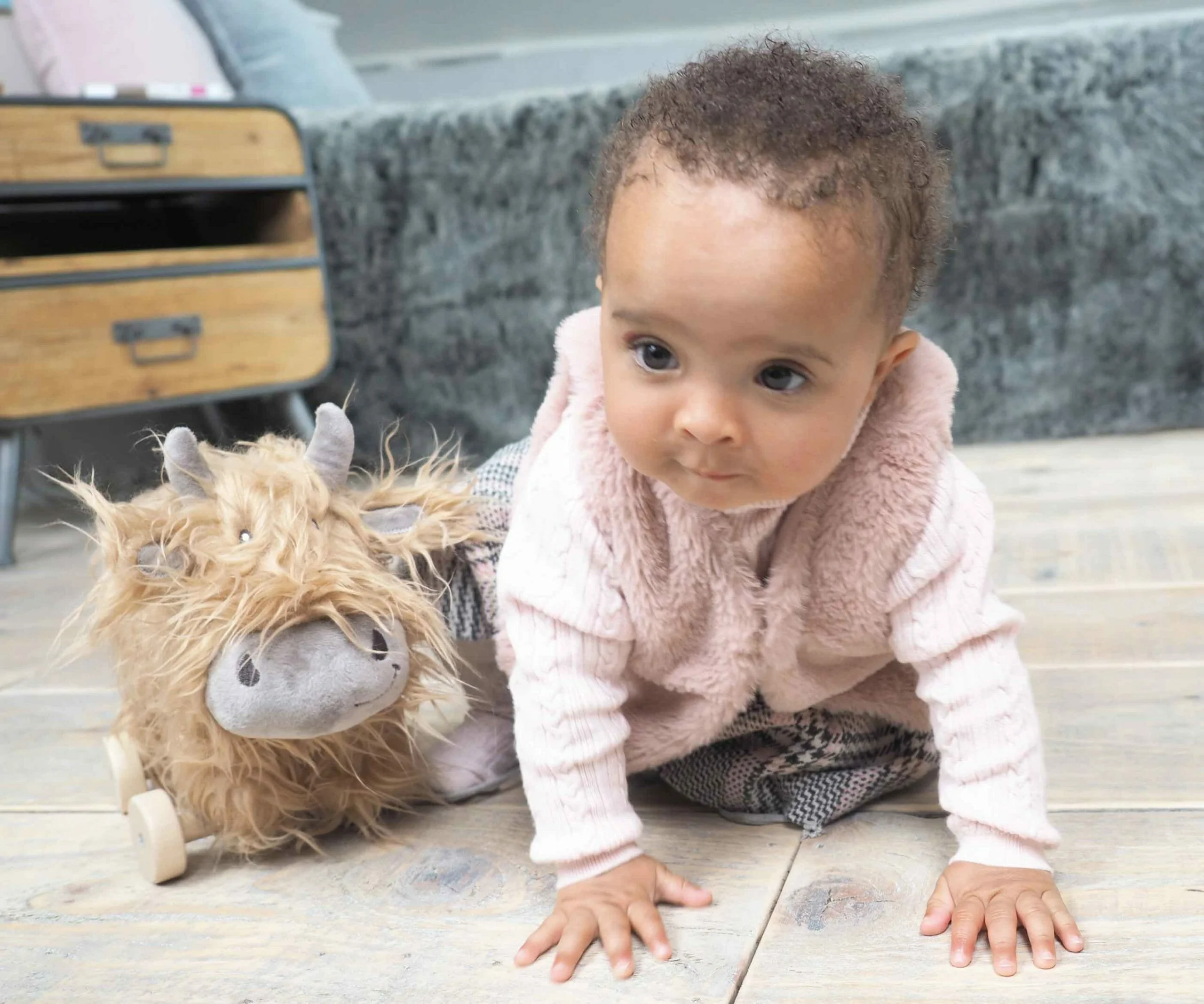 Baby girl crawling alongside Hubert Highland Cow Pull Along Hug Toy