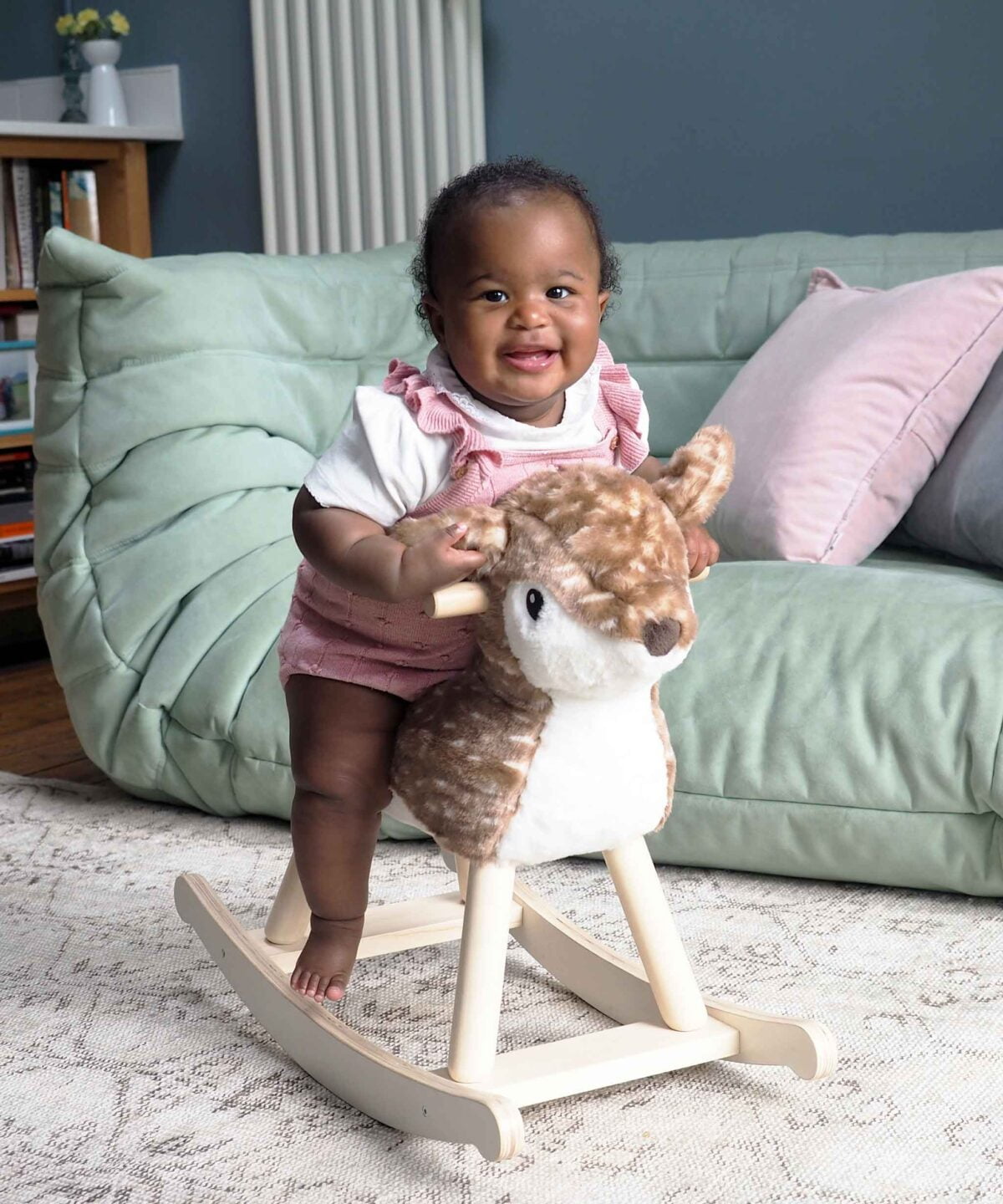 Toddler riding on willow rocking deer toy in front of green sofa