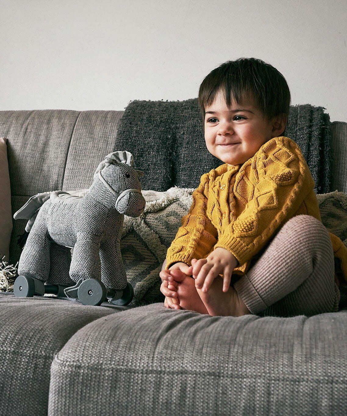 Little girl sat on sofa next to Stirling Horse Pull Along Toy with grey painted removable wheels