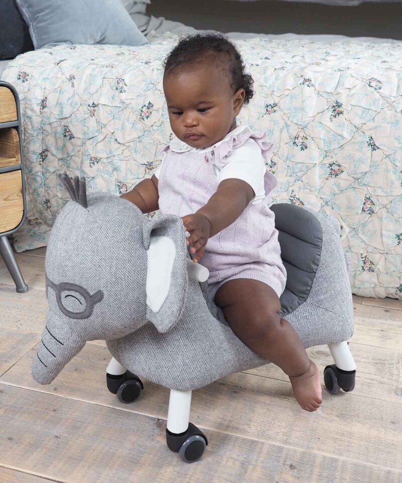 Baby girl riding on Cuthbert Elephant Ride On Toy with grey herringbone fabric