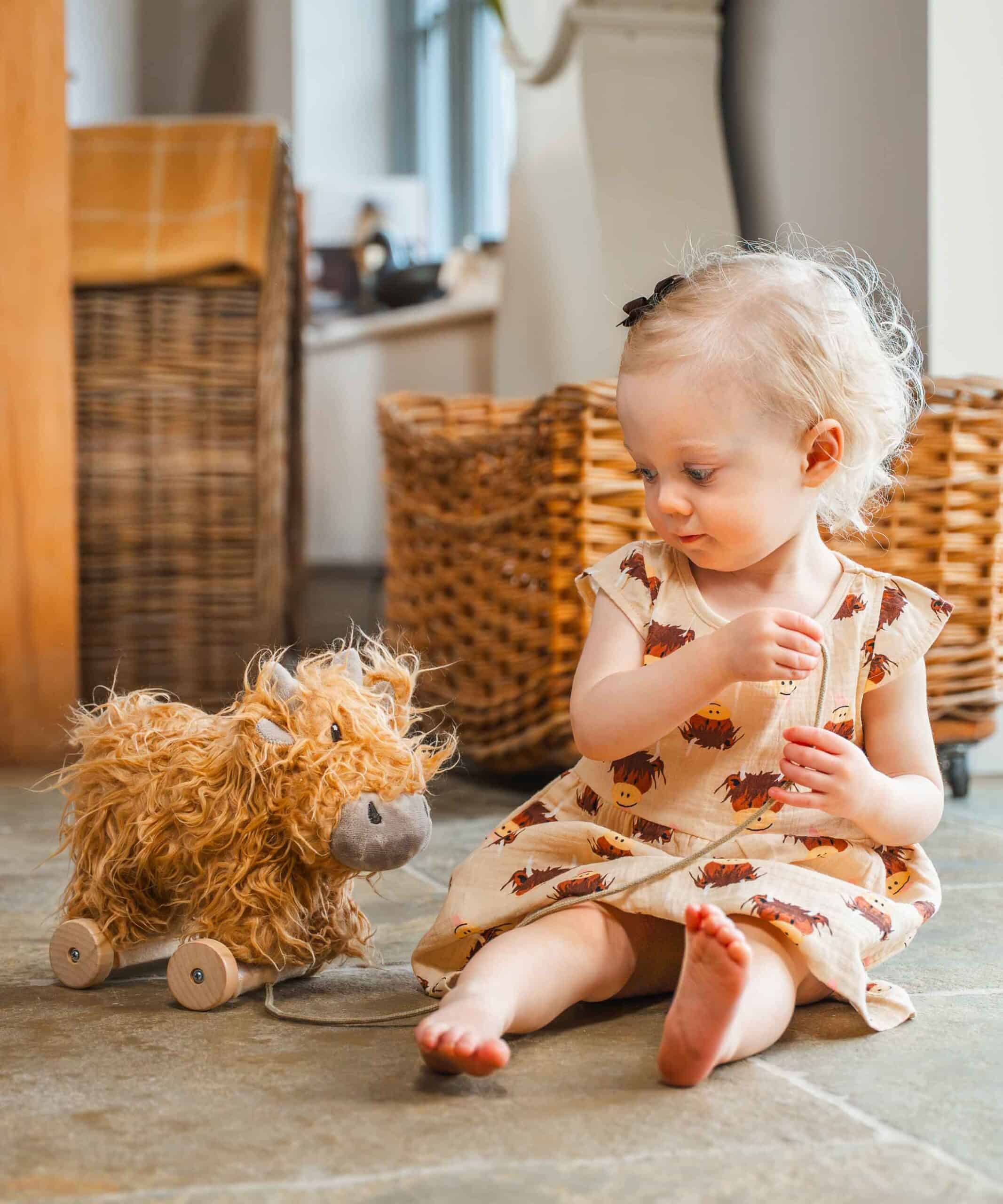 Little girl in a summer dress, playing with her highland cow gift