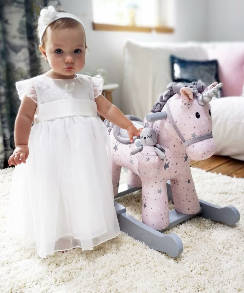 Girl standing next to Celeste & Fae Rocking Unicorn with pink star print fabric and painted wooden rocking rails