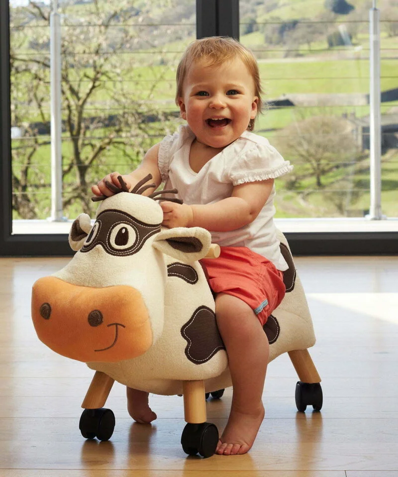 Little girl riding Moobert Cow Ride On Toy on wooden floor