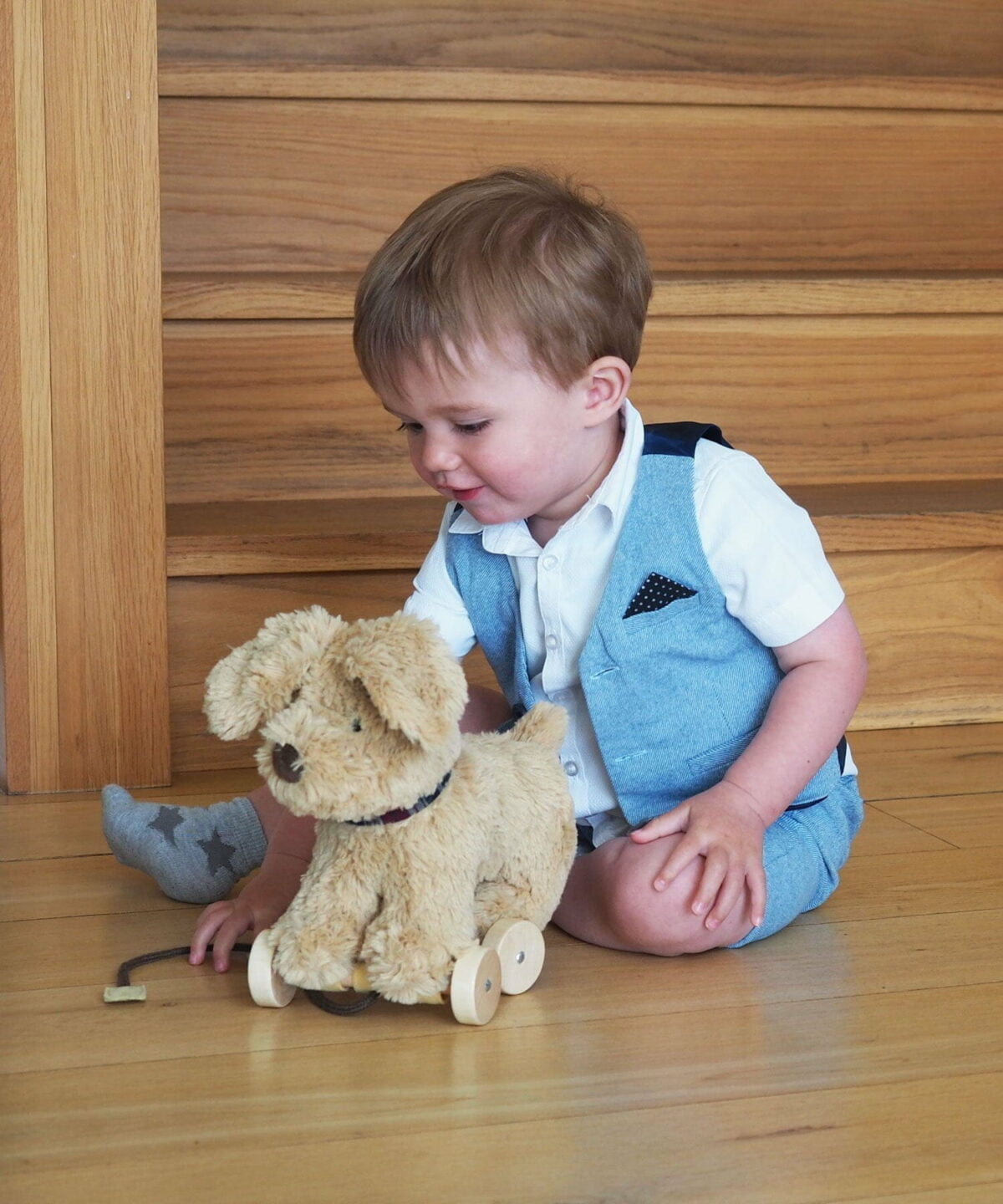 Little boy sits playing with Dexter Dog Pull Along Toy with plush sandy fabric