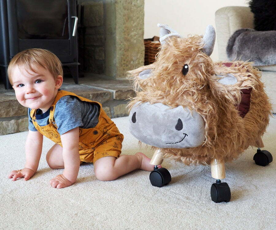 Hubert Highland Cow Ride On Toy with castor wheels stands next to toddler