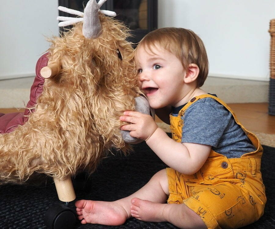 Little boy hugging Hubert Highland Cow Ride On Toy