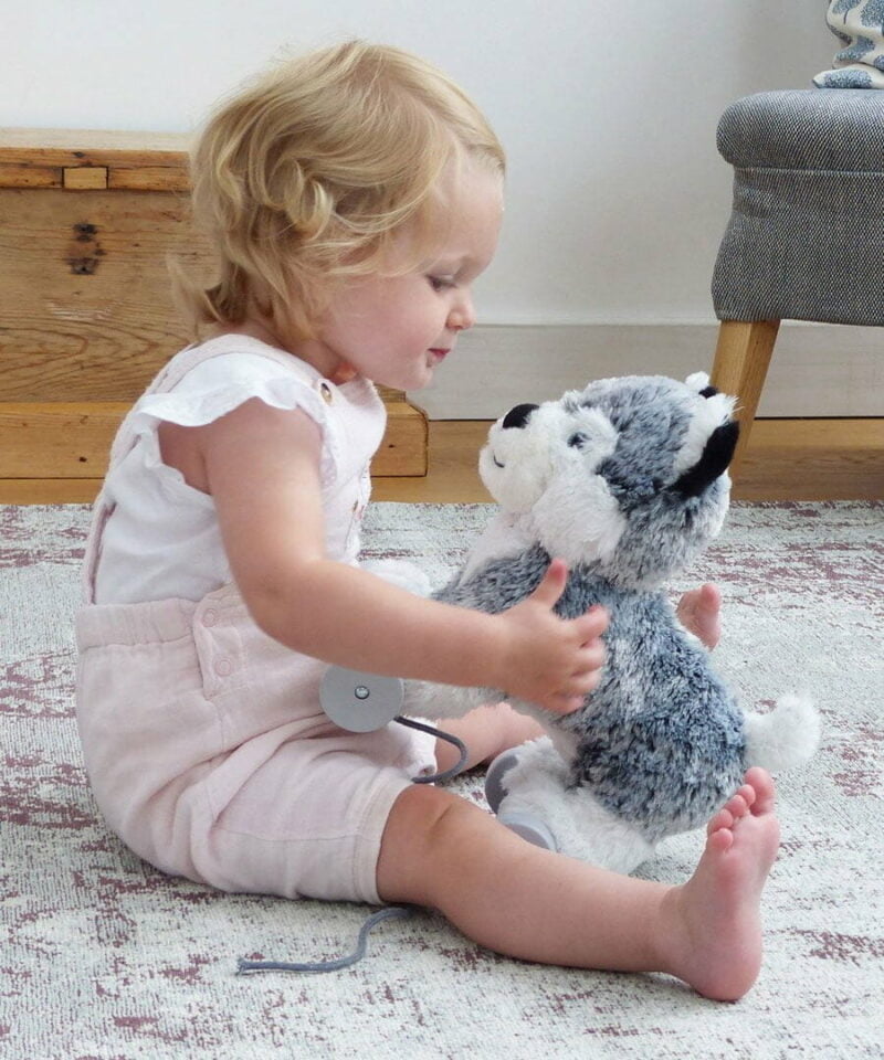 Baby Girl sat with Mishka Dog Pull Along Toy with white and silver plush fluffy fabric