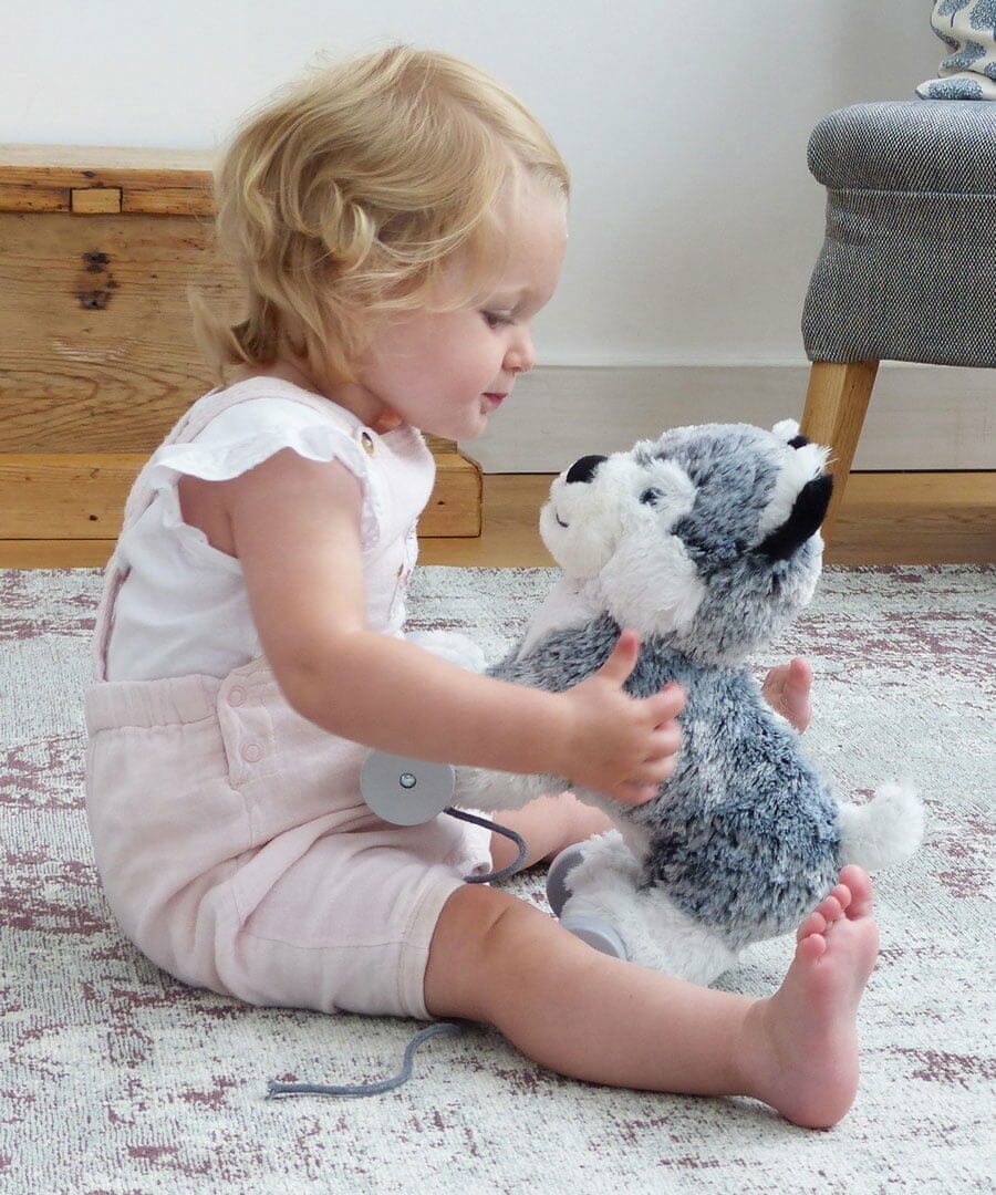 Baby Girl sat with Mishka Dog Pull Along Toy with white and silver plush fluffy fabric