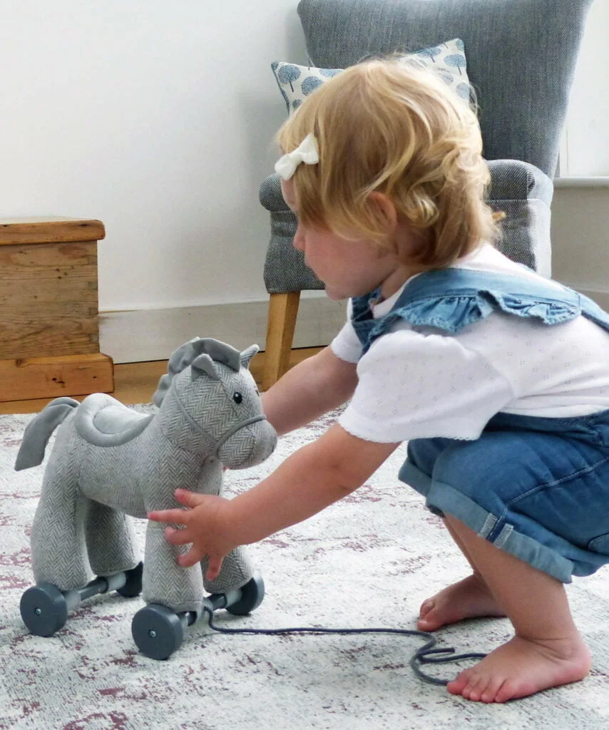 Toddler playing with Stirling Horse Pull Along Toy with grey herringbone fabric