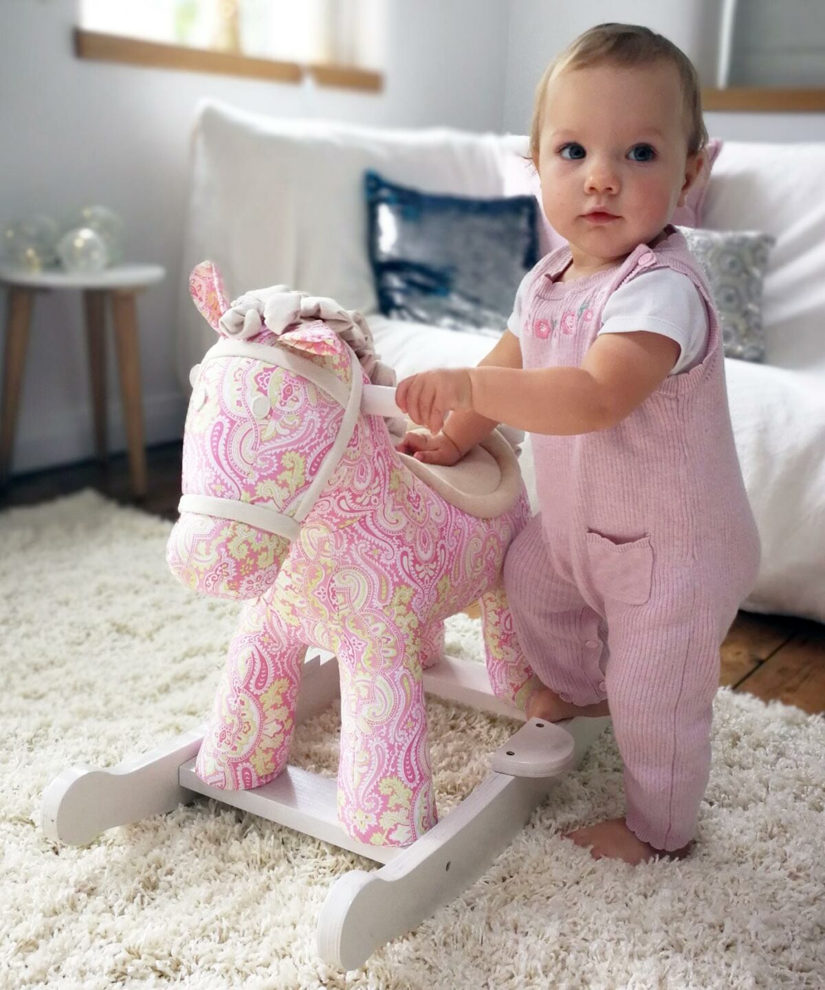 Baby girl standing next to pink Pixie & Fluff Rocking Horse