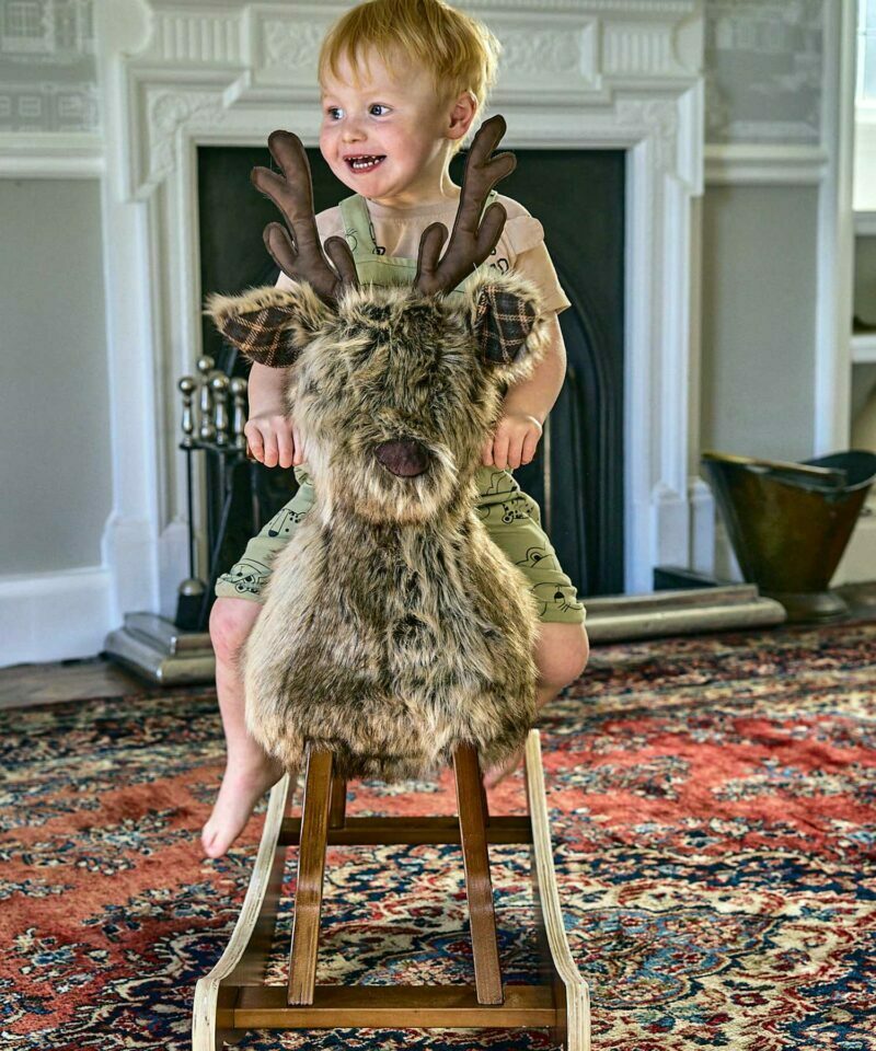 Little boy riding Hamilton Rocking Stag with luxury plush coat in front of fireplace