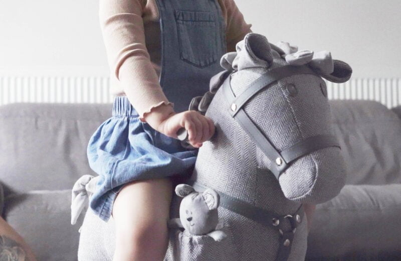 Girl sitting on grey Stirling & Mac Rocking Horse showing leatherette bridle and mac bear pocket toy