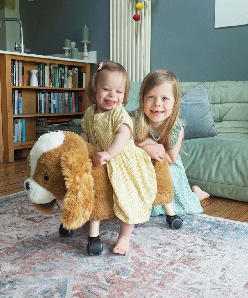 Toddler Girl and Sister playing with Peanut Pup Ride On Toy in living room 