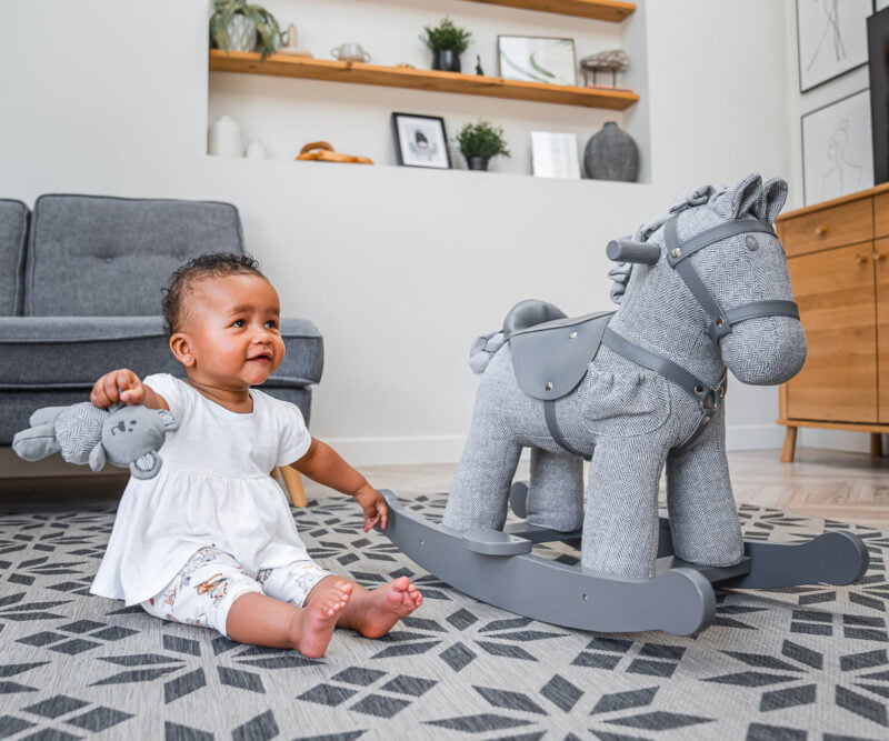 little girl sat with teddy bear next to grey rocking horse for toddlers