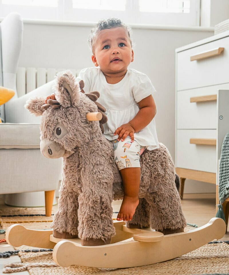 little girl rocking donkey ride on toy in nursery room 