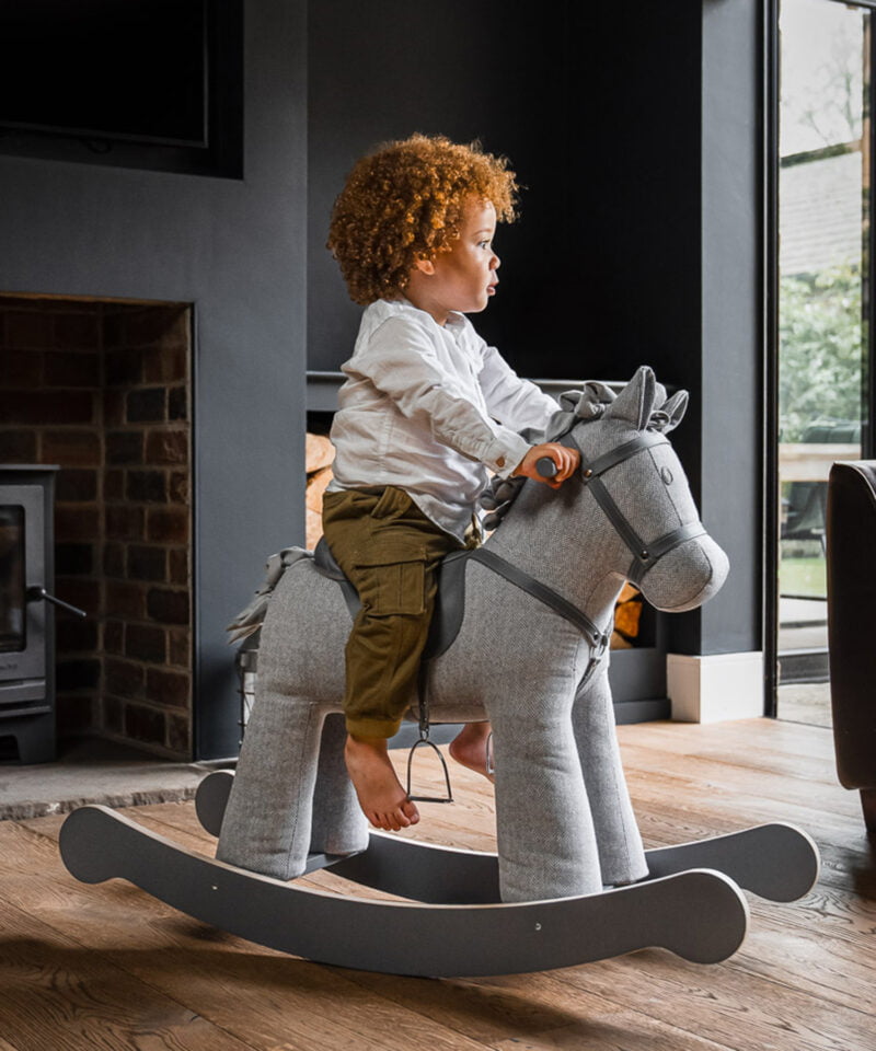 little boy riding on grey rocking horse in living room 