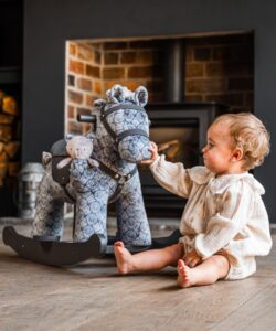 toddler girl sat with blue rocking horse in room 